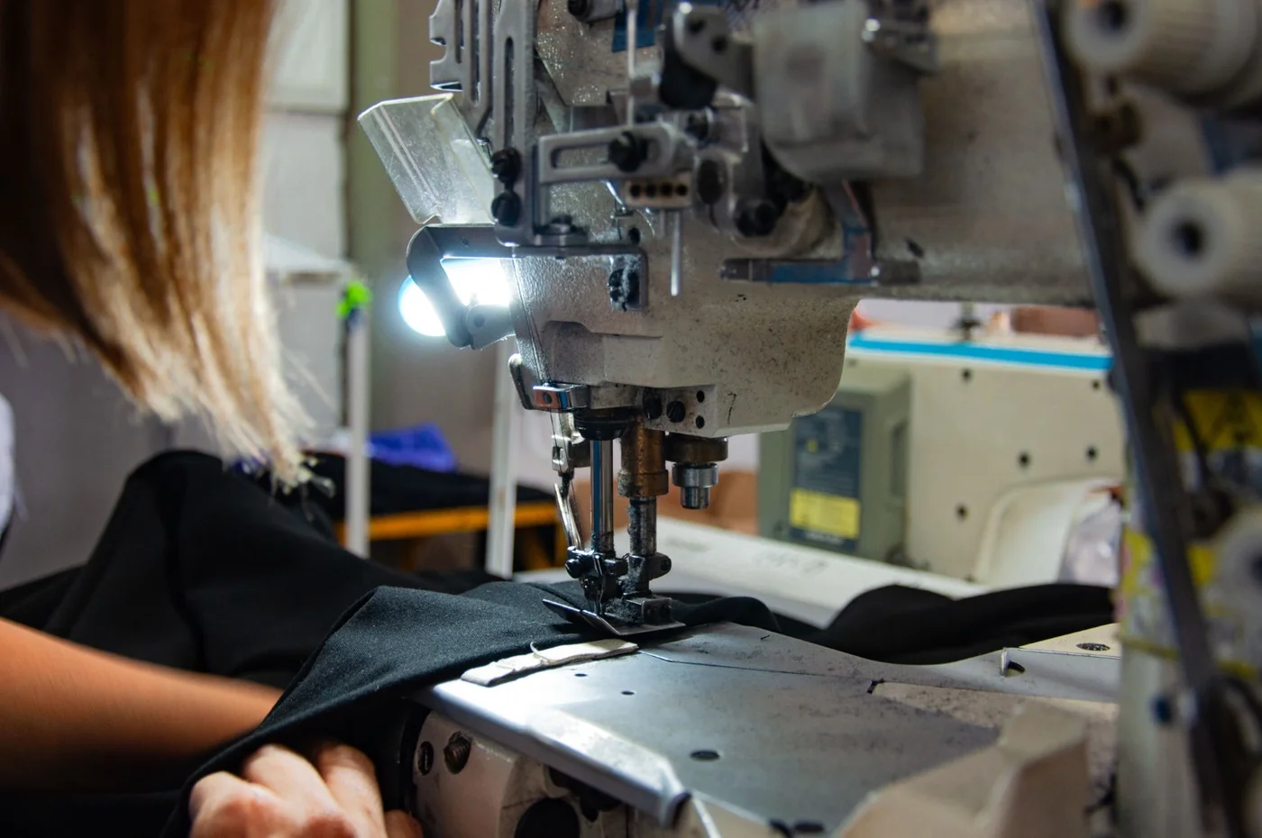 Operator guiding black fabric under the LED-lit needle of an industrial sewing machine