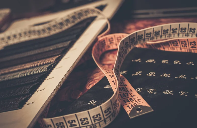 Tailor's measuring tape curled over a fabric swatch book and pattern notes