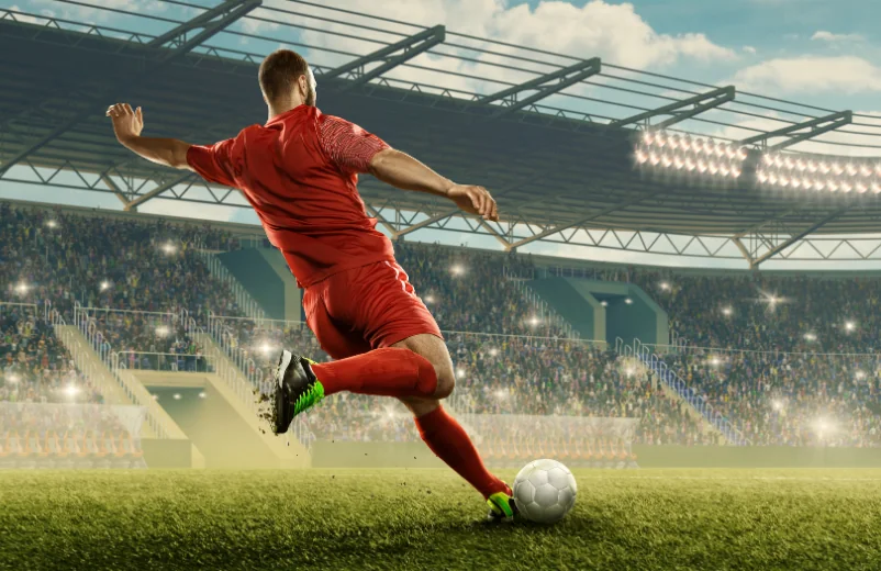 Soccer player in a red kit striking the ball on a stadium pitch