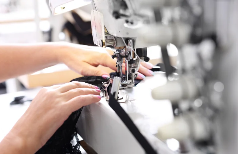 Operator's hands guiding black fabric through an industrial overlock machine