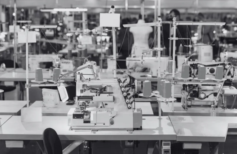 Industrial sewing machines lined up on a factory floor, black and white photo