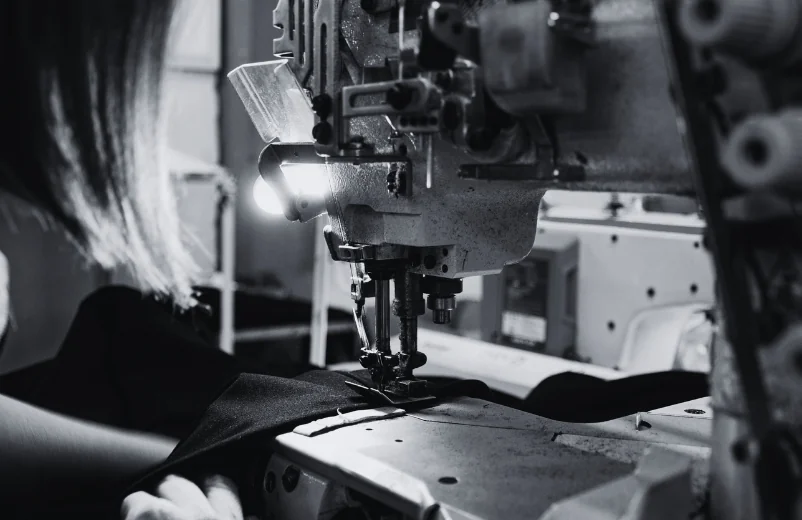 Operator sewing black fabric under the lamp of an industrial machine, black and white photo