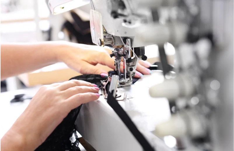 Operator's hands guiding black fabric through an industrial overlock machine