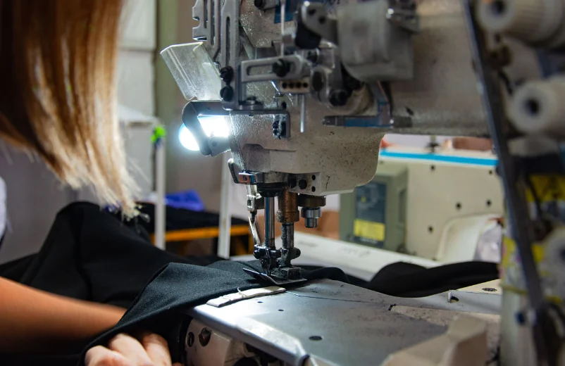 Operator guiding black fabric under the LED-lit needle of an industrial sewing machine