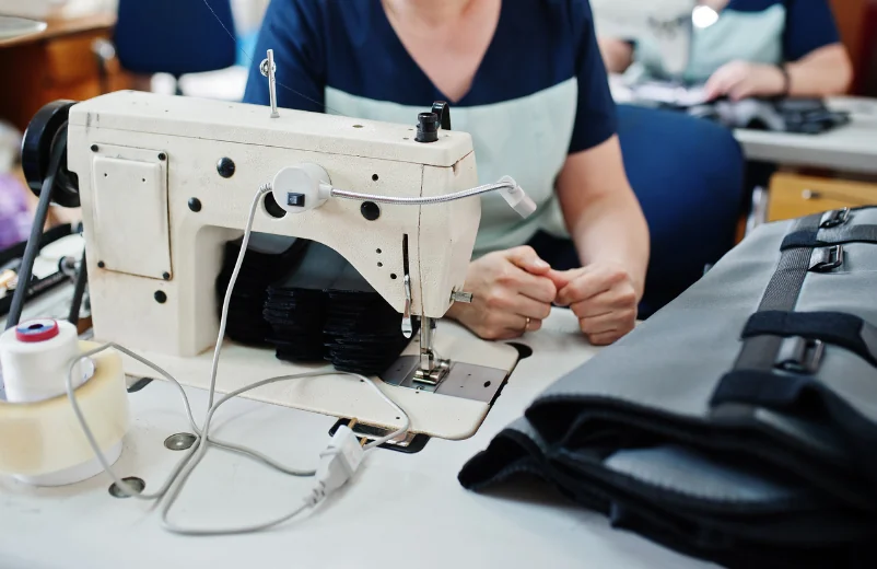 Seamstress sewing a dark garment on a sewing machine in a workshop