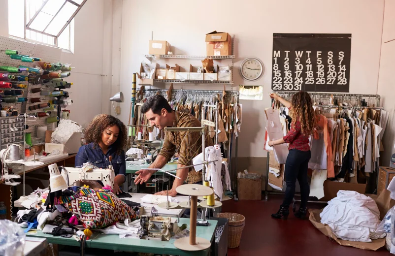 Small studio with a team sewing, cutting and organizing garment racks