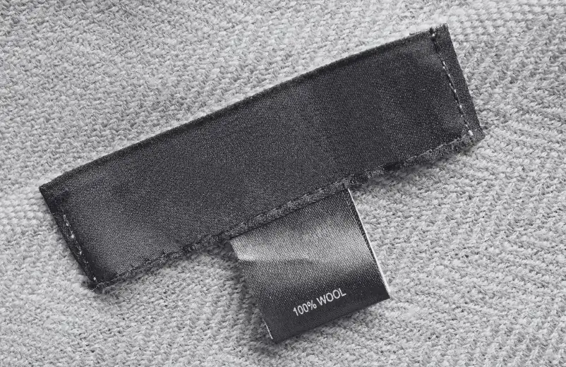 Black care label reading 100% wool on a grey knit garment