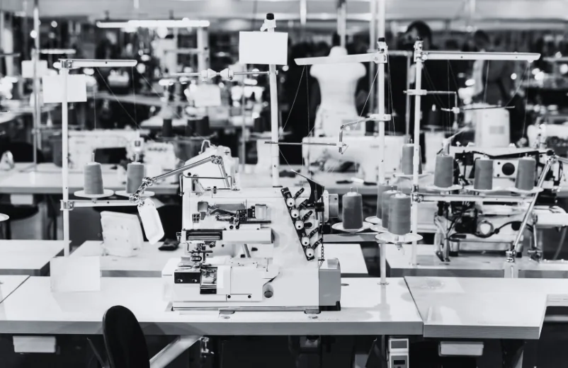 Industrial sewing machines lined up on a factory floor, black and white photo