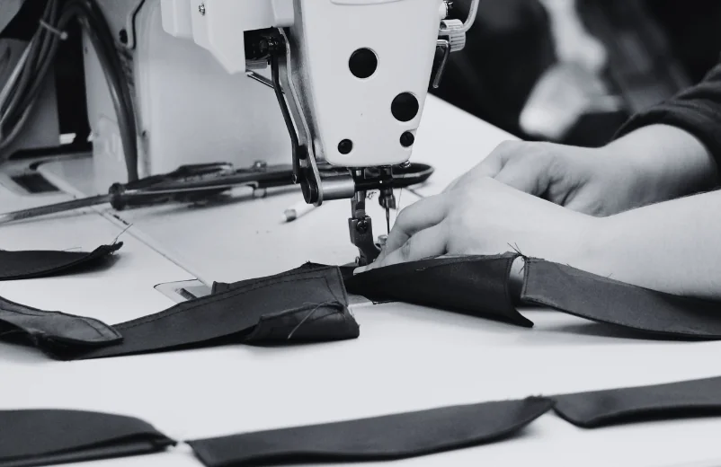Hands sewing black cut pieces on an industrial machine, black and white photo
