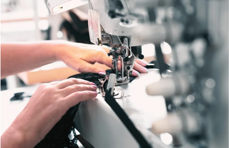 Operator's hands guiding black fabric through an industrial overlock machine