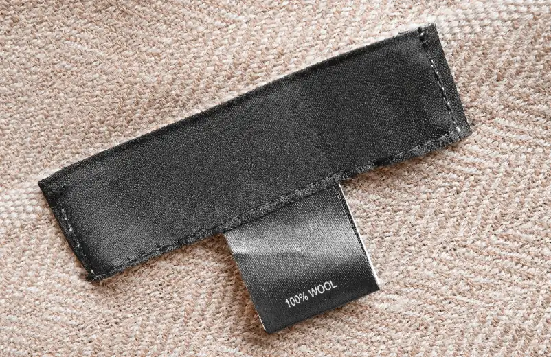 Black care label reading 100% wool on a beige knit garment