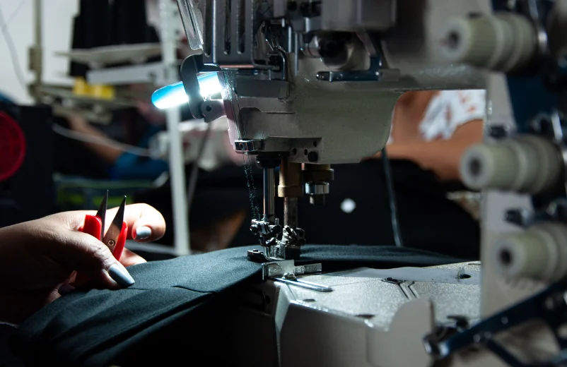 Operator sewing dark fabric under the lamp of an industrial machine