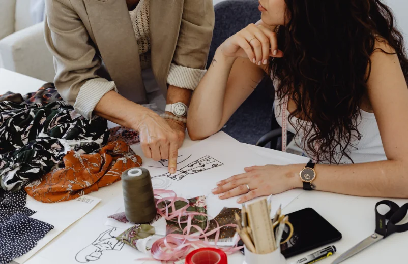 Two women reviewing sketches, fabrics and trims at a design table