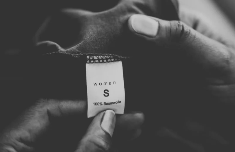 Hand holding a garment label reading woman, size S, 100% cotton, black and white photo