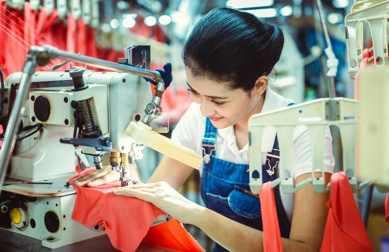 Machine operator sewing a red garment on a factory line