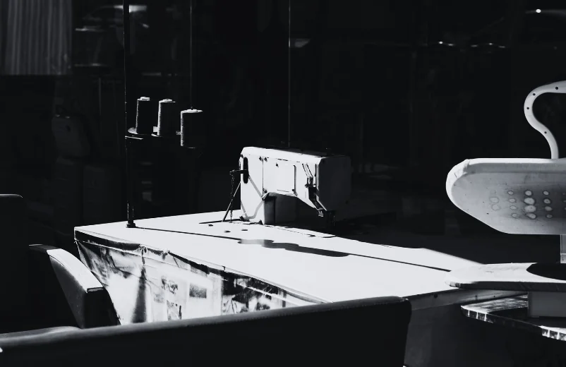 Sewing machine and cutting table in a dim workshop, black and white photo