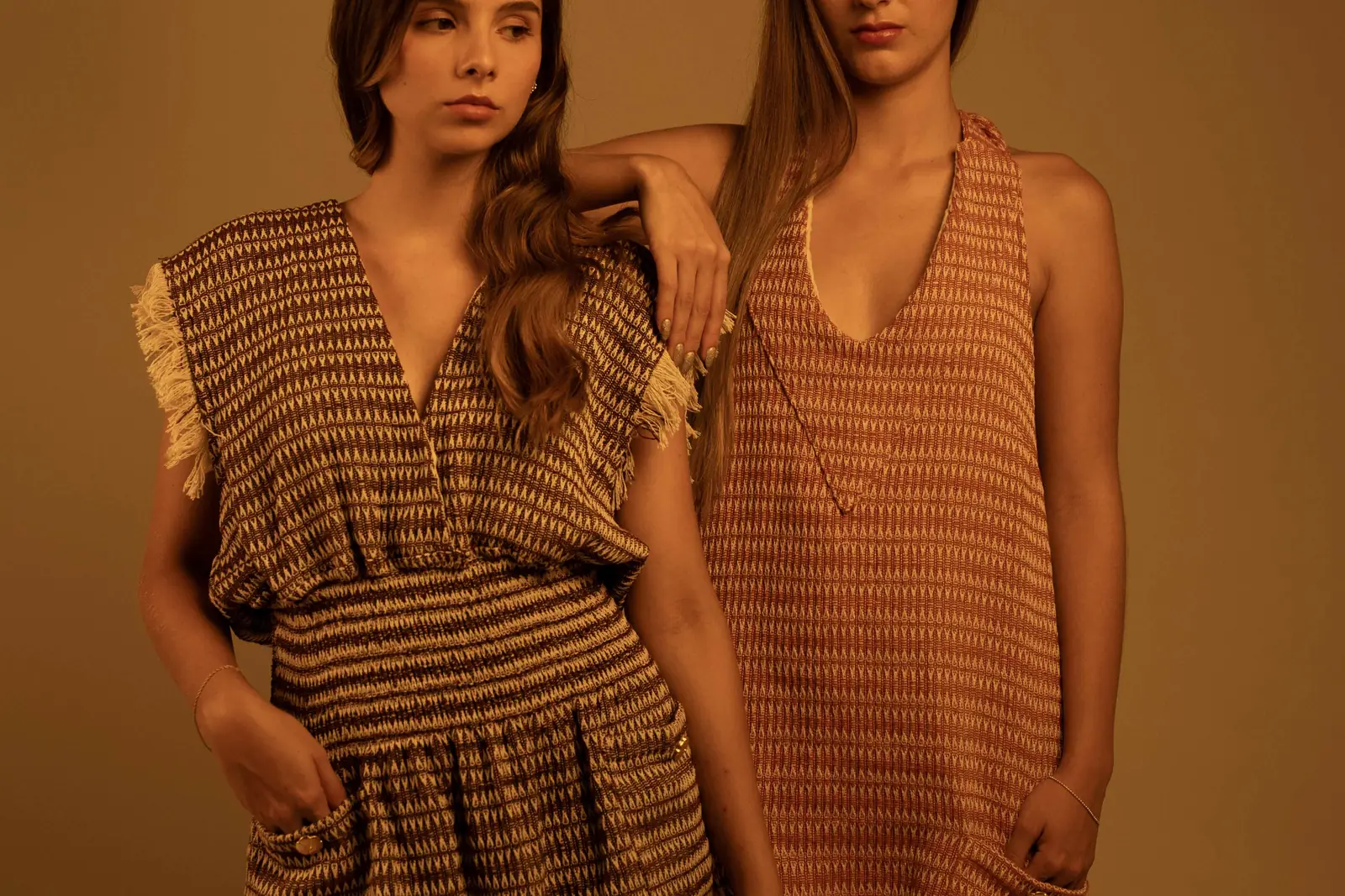Two models in textured fringe dresses manufactured by GAT, in cream and orange