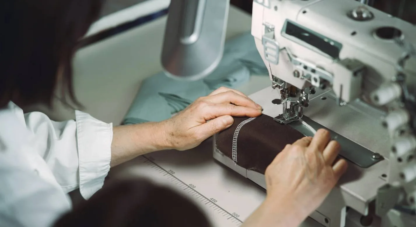 Costurera cosiendo pieza de tela marrón en máquina industrial