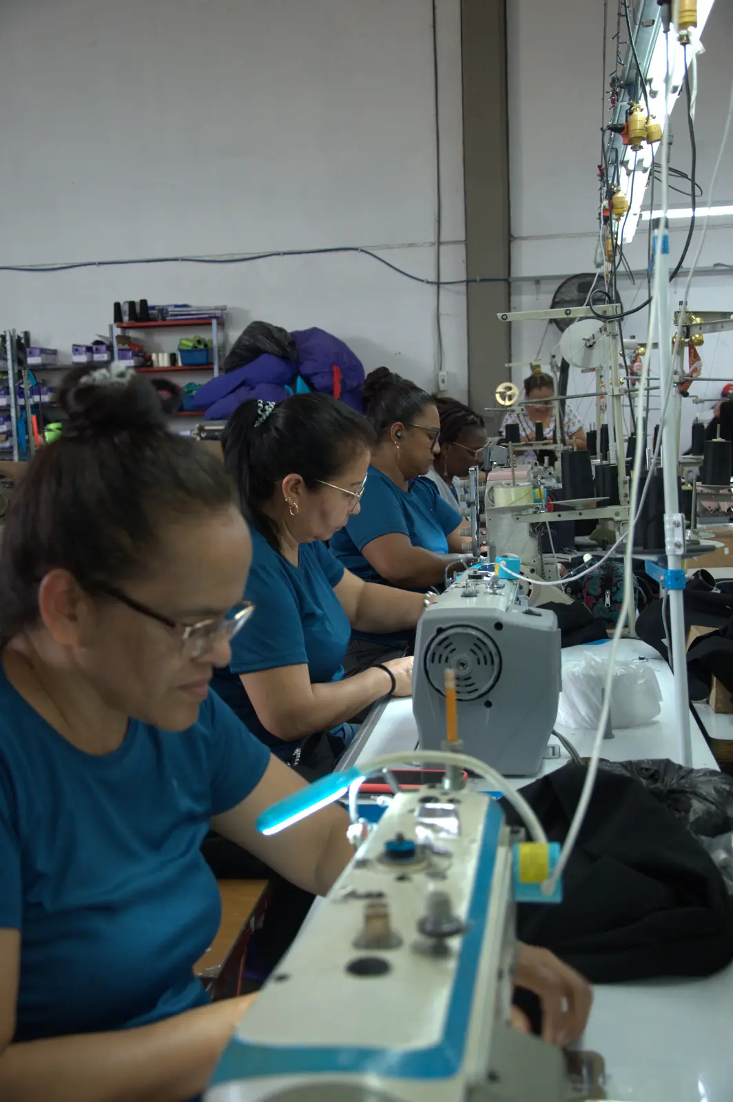Row of workers in teal uniforms sewing on industrial machines at the GAT production line