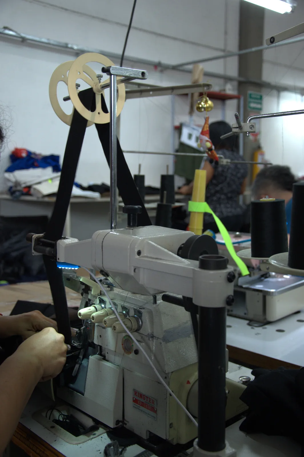 Operator feeding black elastic tape through an industrial overlock machine at a garment workshop