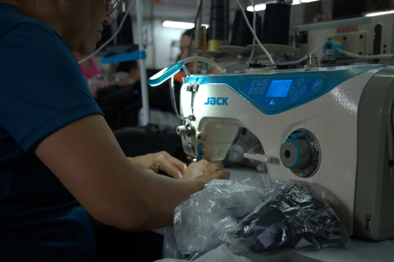 Worker sewing on an industrial machine next to finished black garments packed in plastic