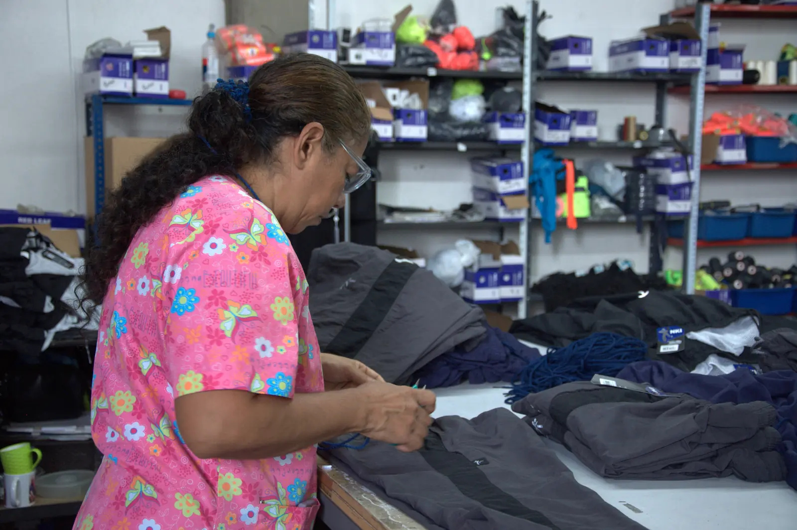 Operaria revisa a mano una prenda gris en la mesa de control de calidad