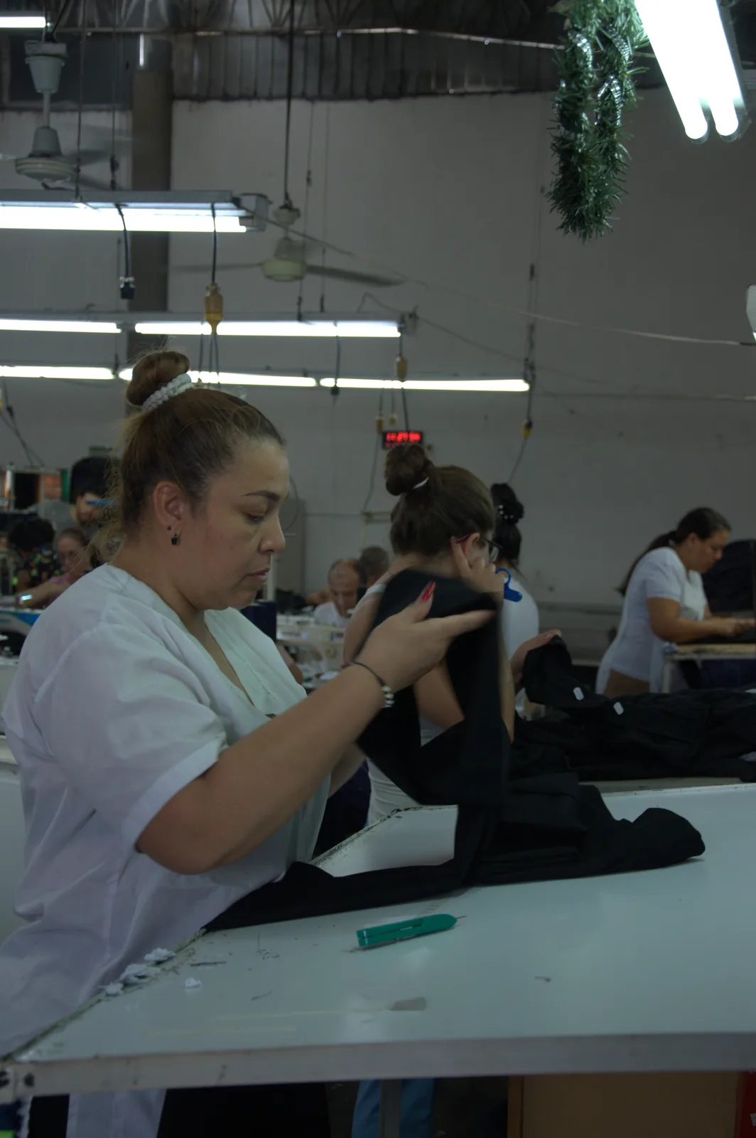 Workers in white smocks folding and handling black fabric on the GAT production floor