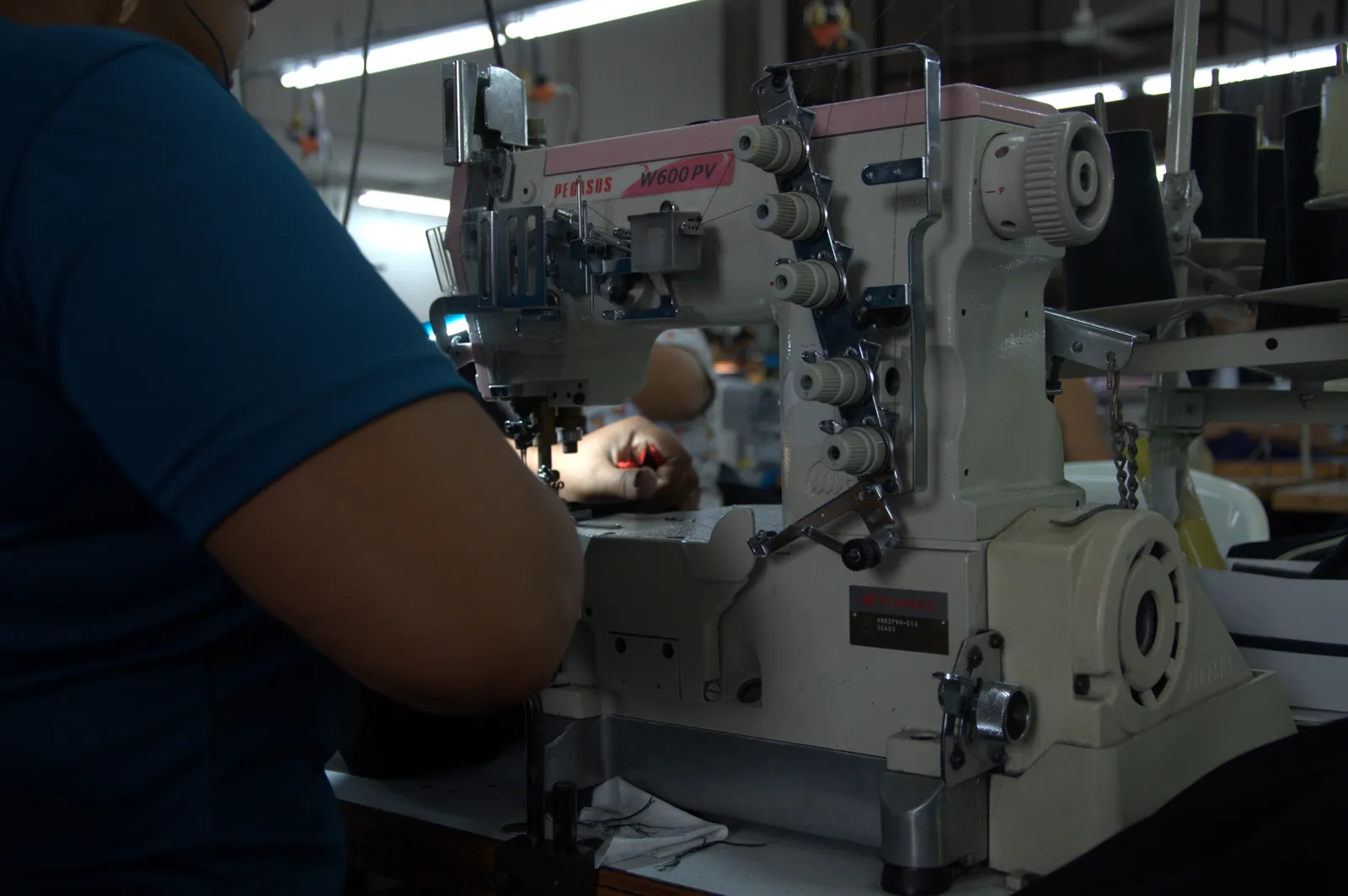 Hands guiding black fabric through an industrial overlock machine on the GAT production floor