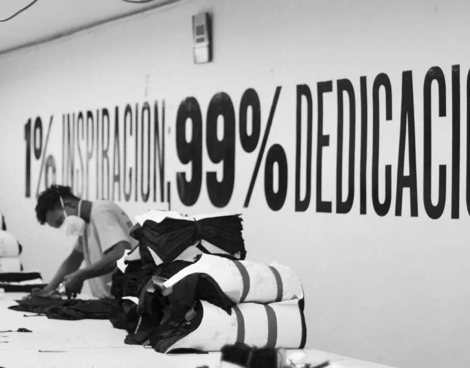 Worker folding fabric beside a wall mural reading '1% inspiration, 99% dedication'